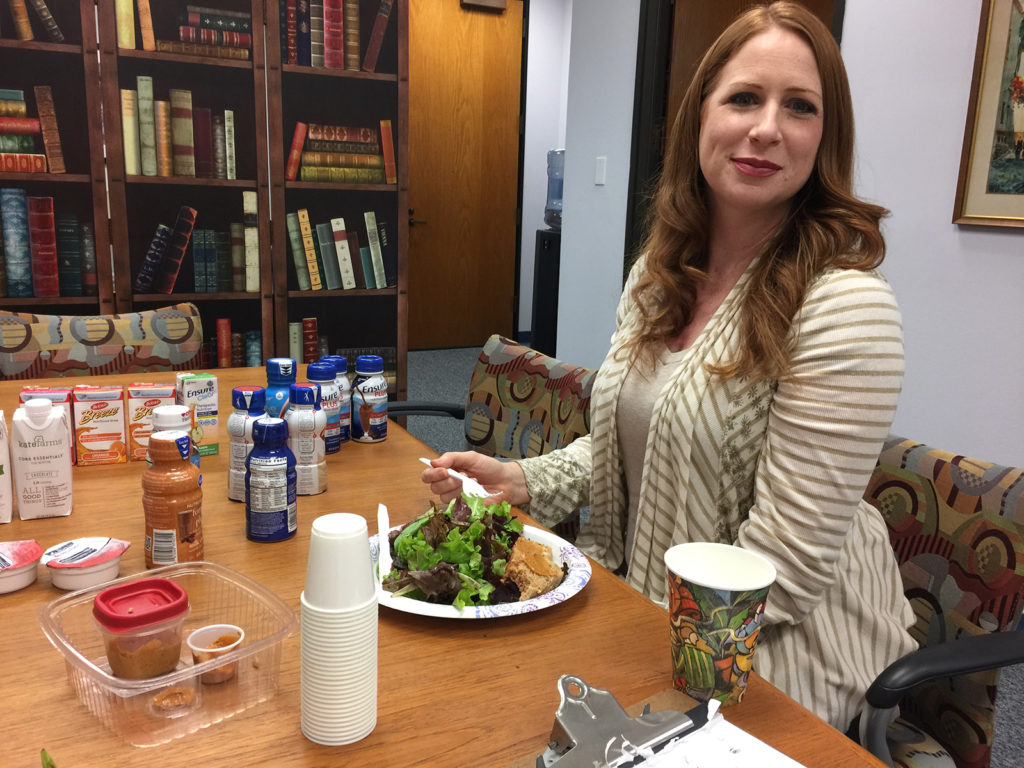 Nutritional Supplements for Eating Disorder Recovery - Katie Grubiak, RDN in Los Angeles, California [Image description: Photo of a smiling, red-headed, white woman, Katie Grubiak, RDN, eating lunch and surrounded by all the nutritional supplements we tasted]