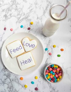 Starting FBT: - Surviving The First Week Family-Based-Treatment for Eating Disorders [Image description: photo of sugar cookies with the words, "Feed, Love, and Heal" on them and colorful candy is in a bowl and scattered around] Represents a potential snack of a teen in eating disorder treatment in Los Angeles, California 