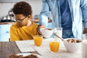 Therapy for ARFID in Children in California [Image description: a boy eating breakfast of cereal and juice and looking unhappy] Represents a potential client receiving counseling for ARFID in California 