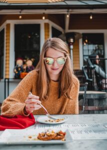 Regular Eating in Eating Disorder Recovery in Los Angeles, California [Image description: a woman eating dessert outside at a restaurant] Depicts a potential client with an eating disorder seeking counseling in California