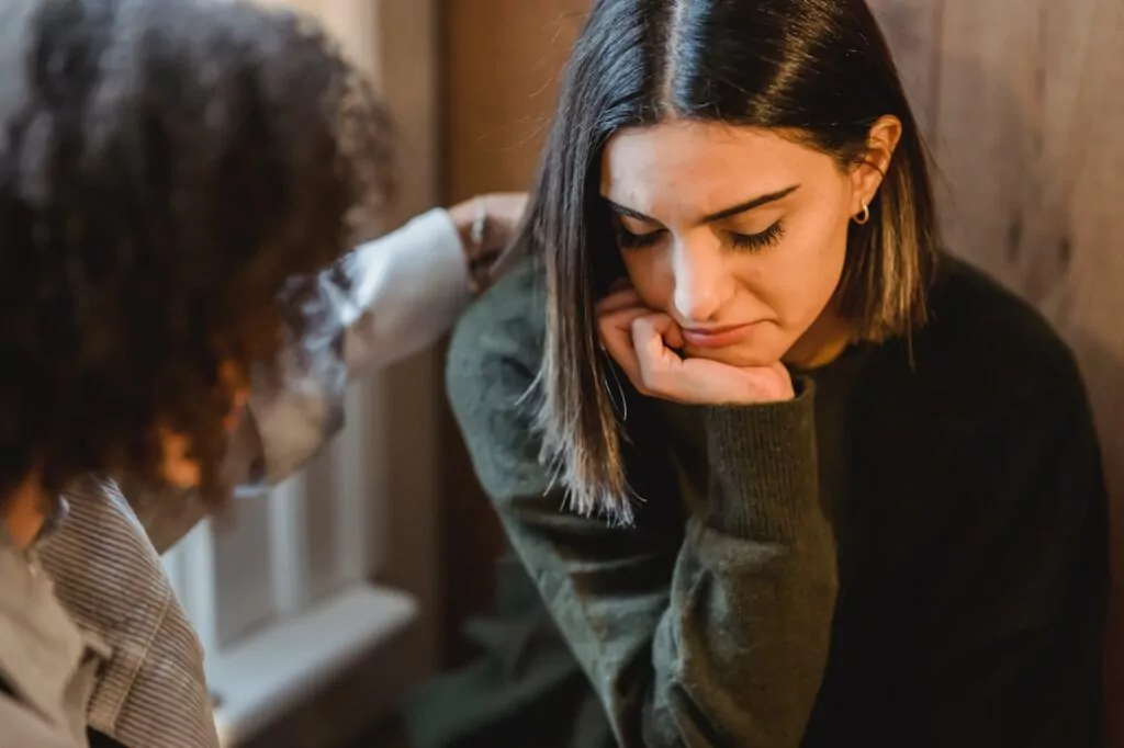 Supporting a friend with ARFID in California [Image description: a woman with her hand on the shoulder of another woman who appears distressed] Represents a potential client getting help for ARFID in California