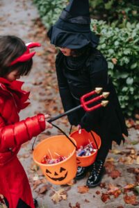 Halloween candy and intuitive eating [Image description: 2 young children in costumes hold pumpkin pails of candy they've collected on Halloween}