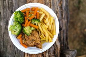 How much food to food during FBT? [Image description: plate of food containing chicken, fries, broccoli, and carrots] Depicts potential plate for teen in recovery