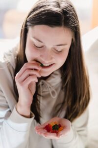 Teen vegetarian [Image description: teen girl with long brown hair eating a handful of gummy candy] Represents a teen girl in California eating a broad range of food