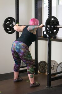Exercise in Eating Disorders [Image description: photo of a mid-size woman with pink hair lifting heavy weights in a gym]
