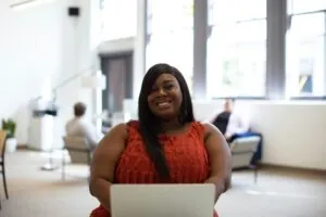 Potential Bariatric Surgery Client in Californai [Image description: a black woman in a larger body smiling and sitting in a waiting room]