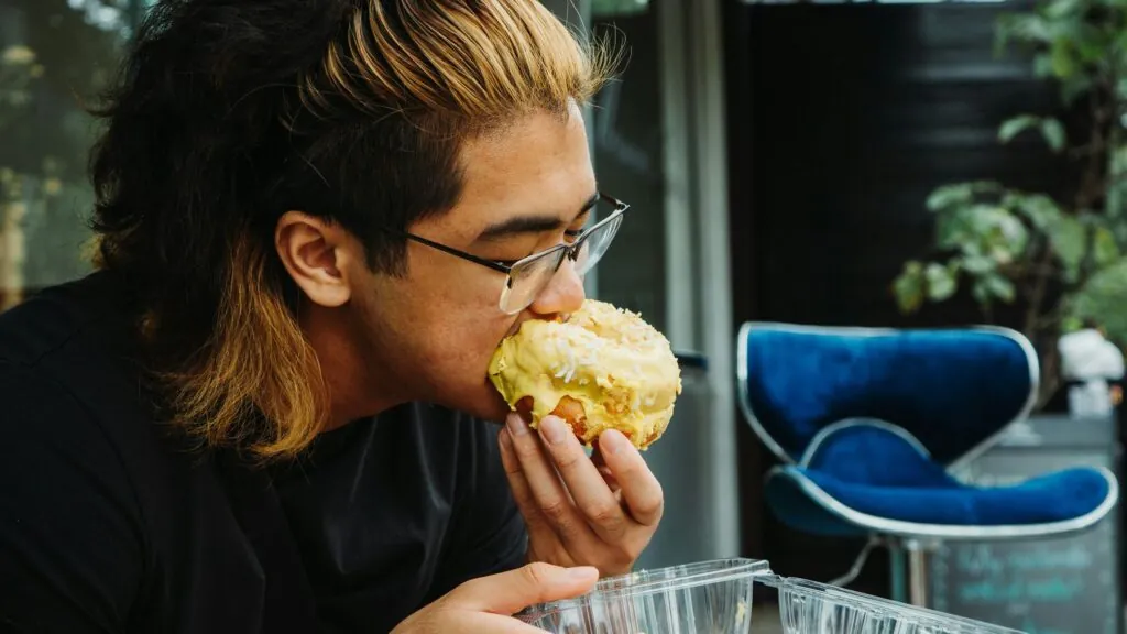 Stop Binge Eating by Eating More [Image description: photo of a young man eating a pastry; represents a potential person in California who is binge eating]